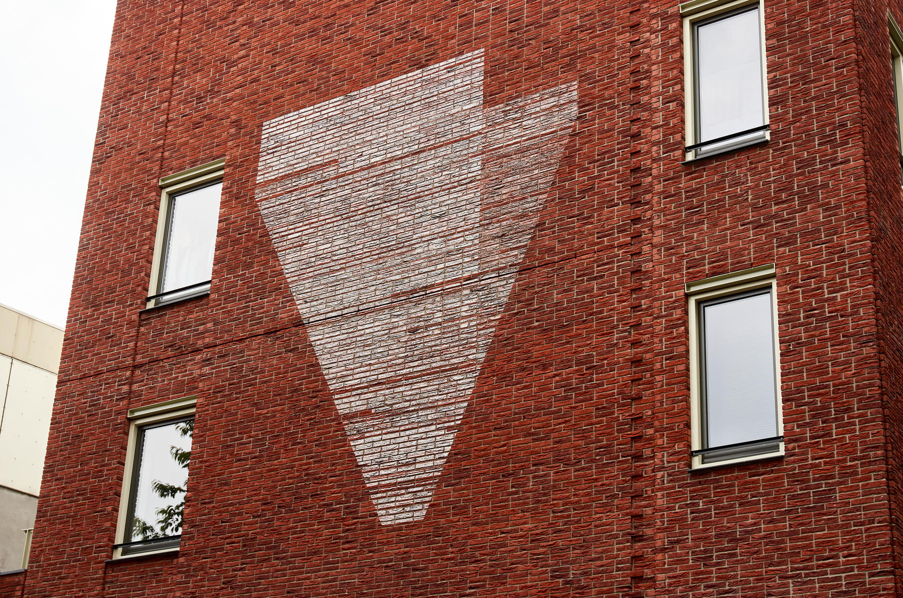 Triangular shaped chalk linedrawing on the brick sidewall of a house, in between 4 windows